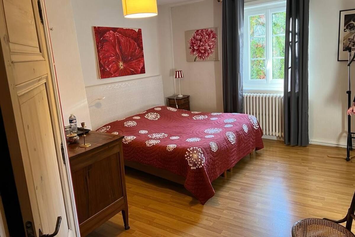 Een slaapkamer met een houten bed, een nachtkastje, een lamp en een raam met gordijnen.