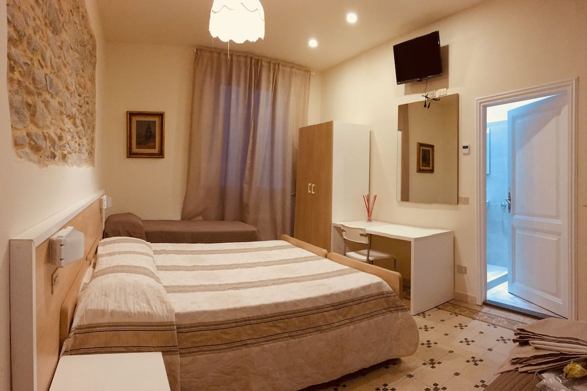 Un dormitorio con cama, escritorio, silla, televisor y puerta.