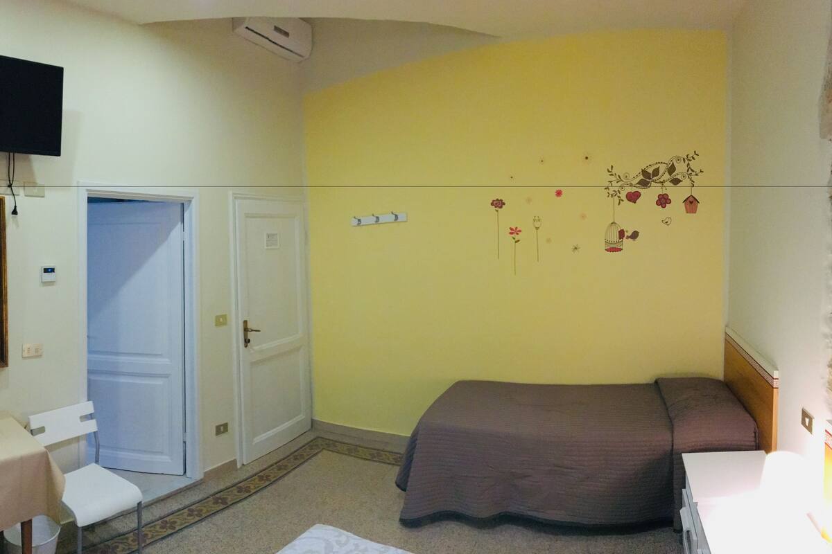 Un dormitorio con cama, escritorio, silla, televisor y puerta.
