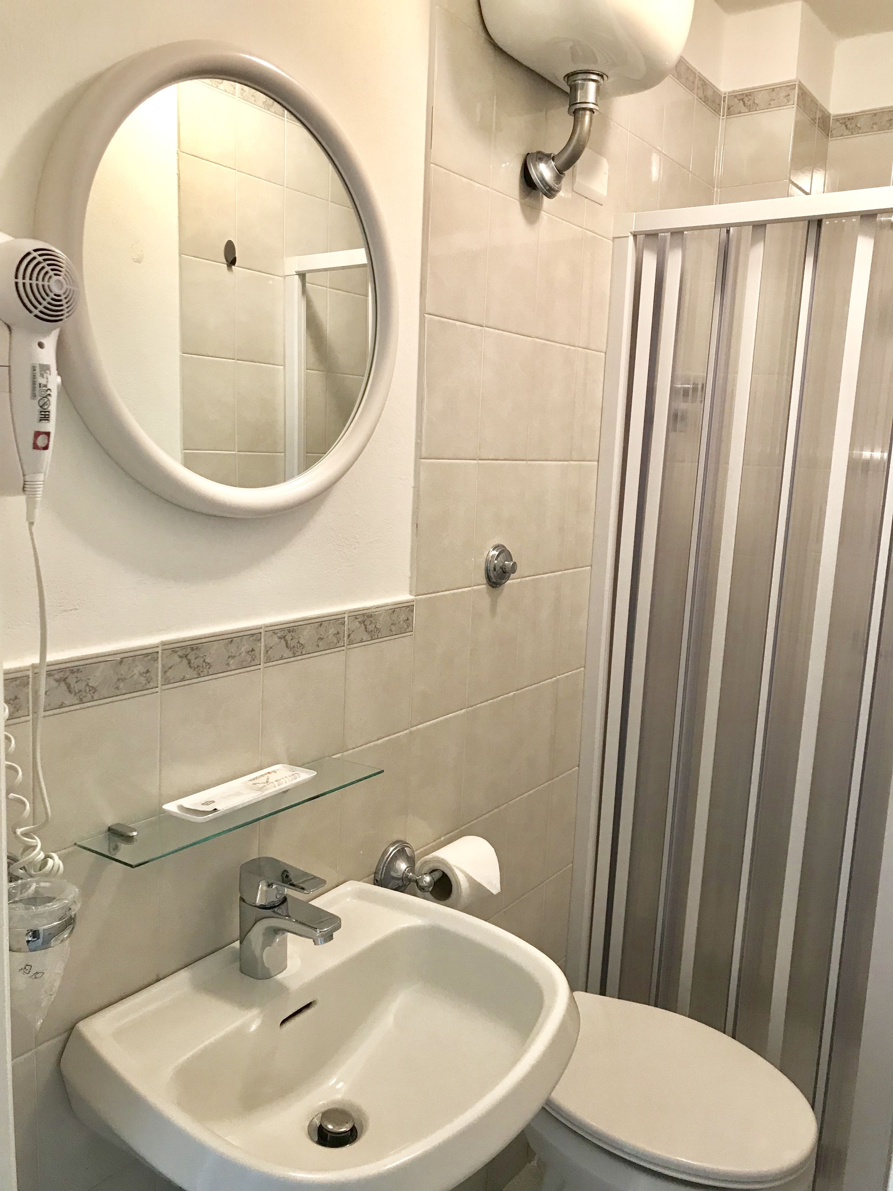 Un bagno con uno specchio rotondo, un lavandino, un water e una doccia con strisce verticali.