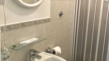 Un bagno con uno specchio rotondo, un lavandino, un water e una doccia con strisce verticali.