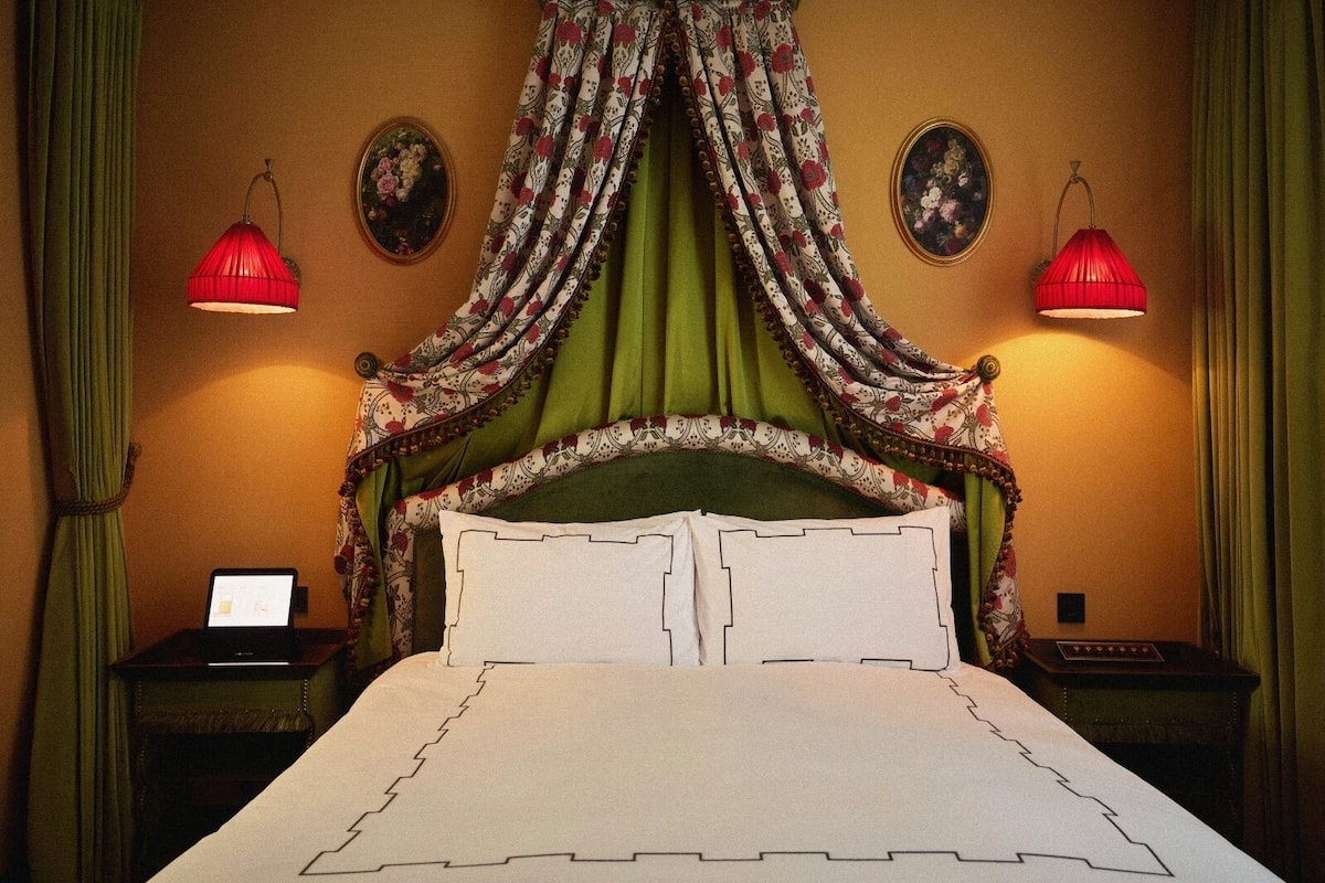 A bedroom with a canopy bed, two bedside lamps, and a nightstand with a lamp.