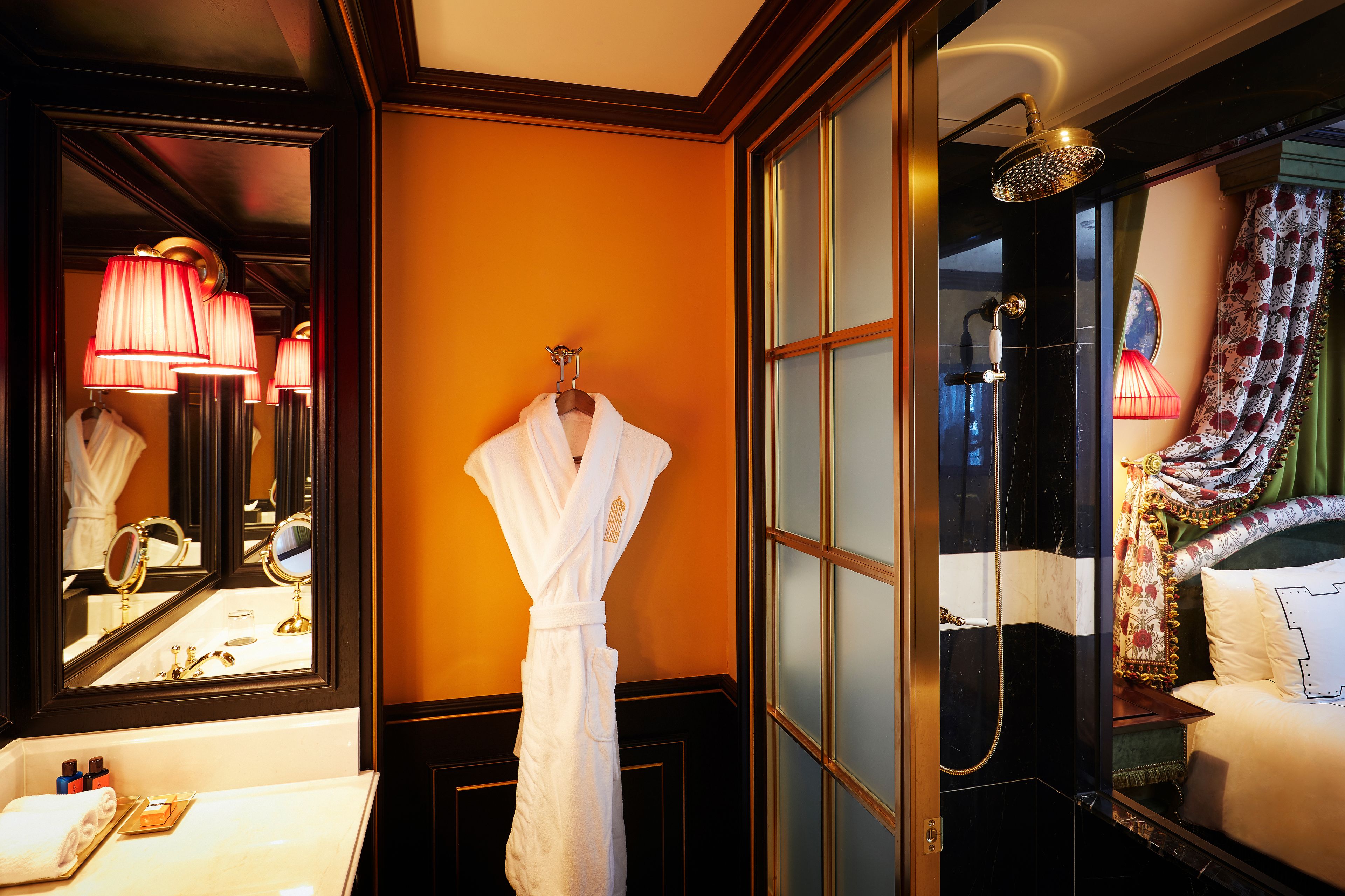 A bathroom with a bathtub, a mirror, a robe hanging on the wall, and a sink with toiletries.