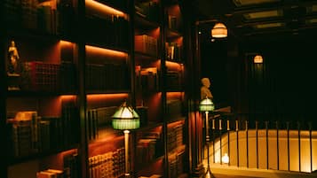 A dimly lit library with bookshelves and two green lamps.