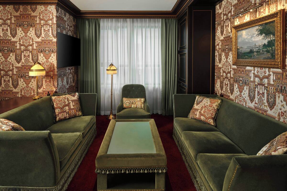 A room with patterned wallpaper, a green sofa set, a coffee table, a floor lamp, and a painting on the wall.