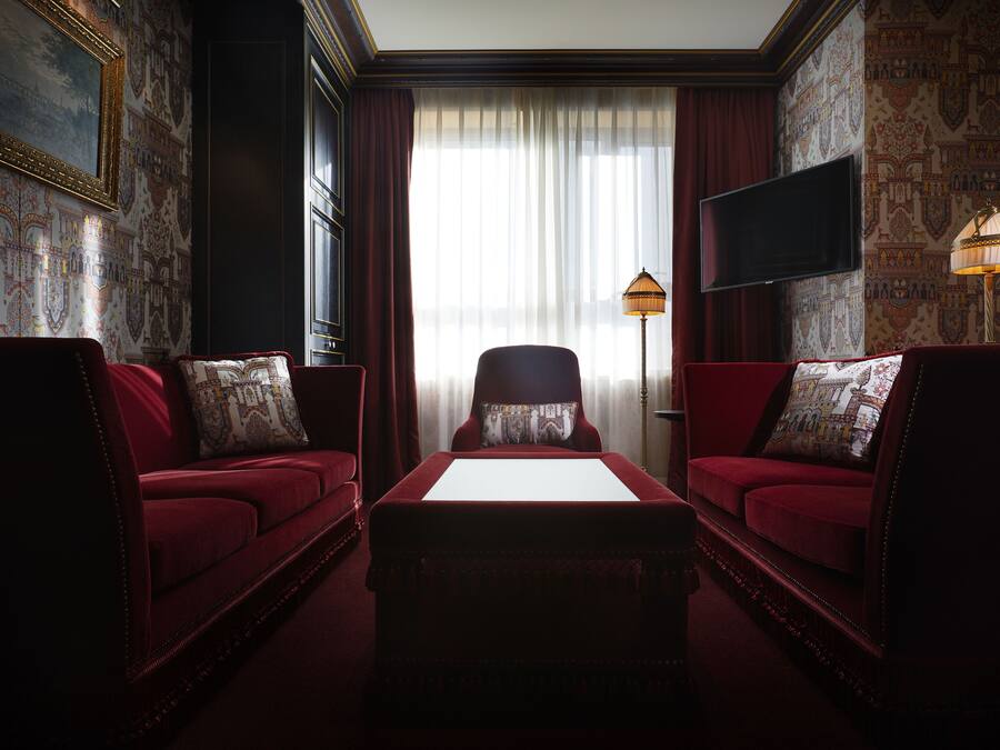 Una habitación con dos sofás rojos, una mesa blanca, un televisor y un papel tapiz estampado.