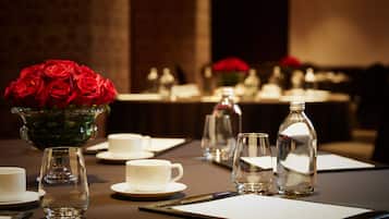 A table set for a meeting with a vase of red roses, clear glasses, and white cups.