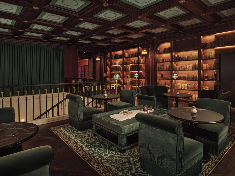 Una biblioteca con estanterías, asientos tapizados en verde y una escalera.