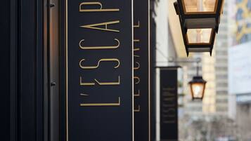 Un letrero negro con letras doradas que dice 'L'ESCAPE' en la fachada de un edificio.