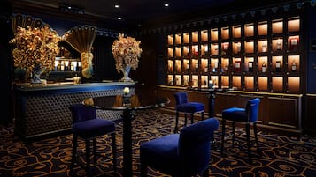 A bar area with a round table, four blue bar stools, and a wall of illuminated bottles.