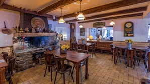 A rustic interior with exposed wooden beams, a brick fireplace, and wooden tables and chairs. - Hôtel Franz (Allos)