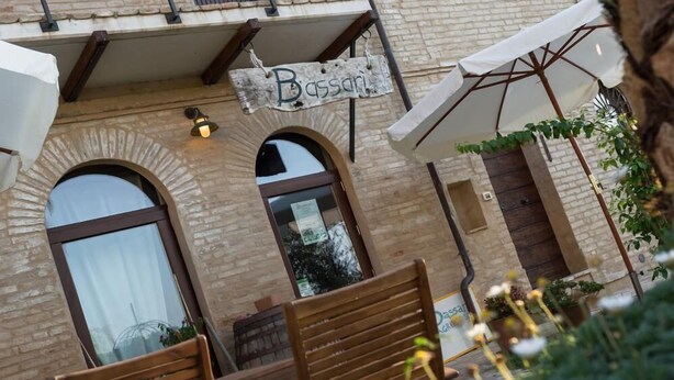 A building with a sign reading "Bassa," featuring a brick facade, arched windows, and a balcony with a metal railing. - Agriturismo Bassarì (Recanati)