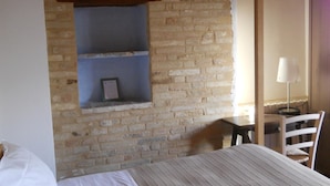 A bedroom with a brick wall, a bed, a desk with a chair, and a lamp. - Agriturismo Bassarì (Recanati)
