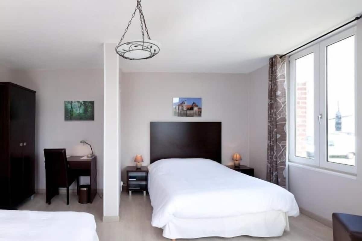 A hotel room with a bed, desk, chair, wardrobe, and a view of the city through the window.