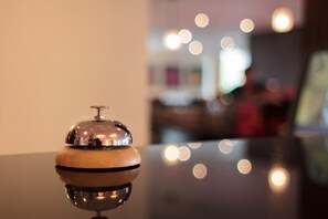 Une table en bois poli, sur laquelle repose un objet métallique réfléchissant, vraisemblablement une clochette d’hôtel, dans un intérieur chaleureux et bien éclairé.