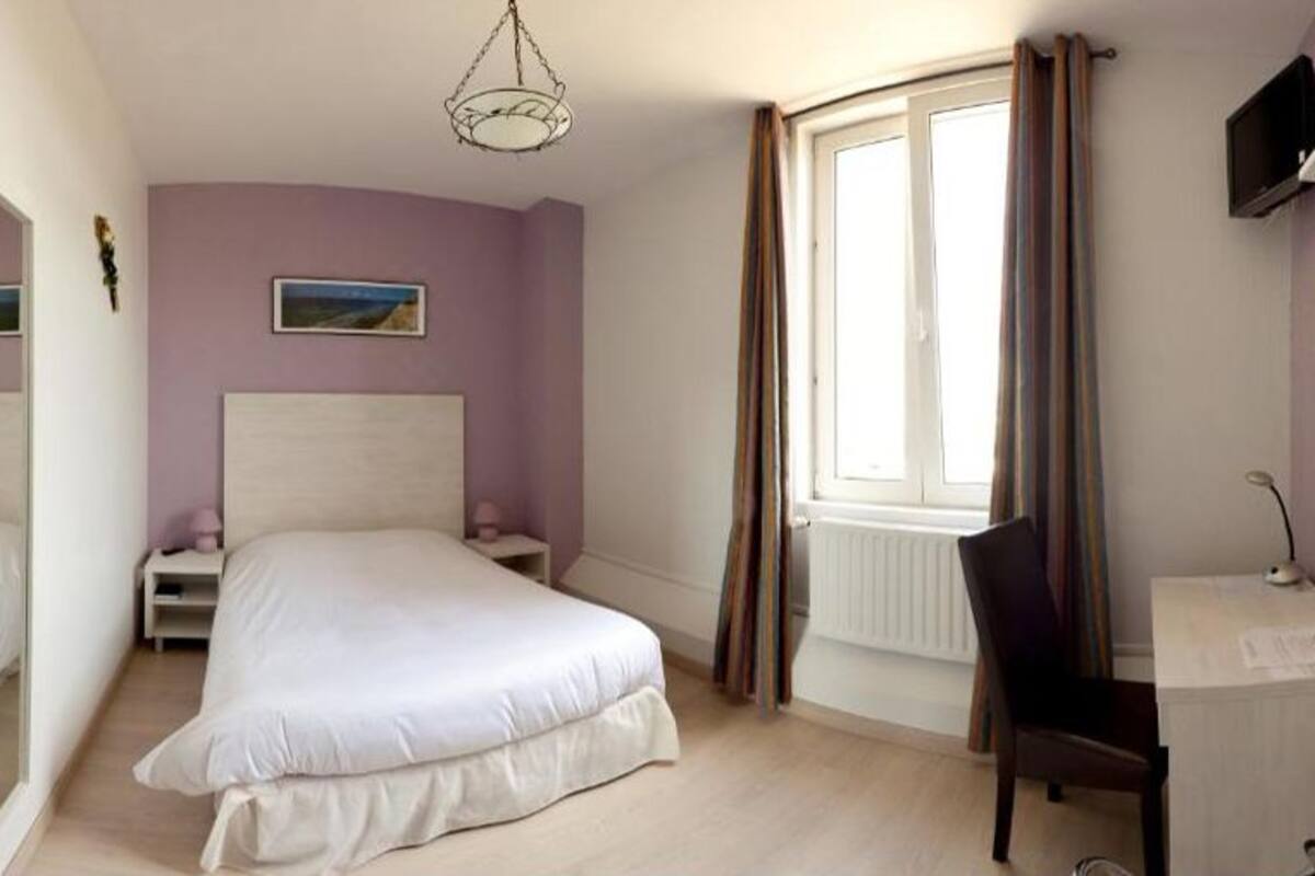 A bedroom with a bed, a desk, a chair, a window with curtains, a television, and a mirror.