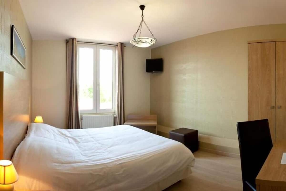 A hotel room with a bed, a desk, a chair, a television, and a wardrobe.