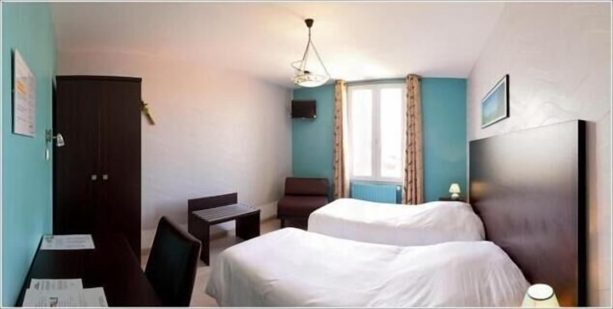 A hotel room with two beds, a desk, a chair, a window with curtains, and a hanging light fixture.