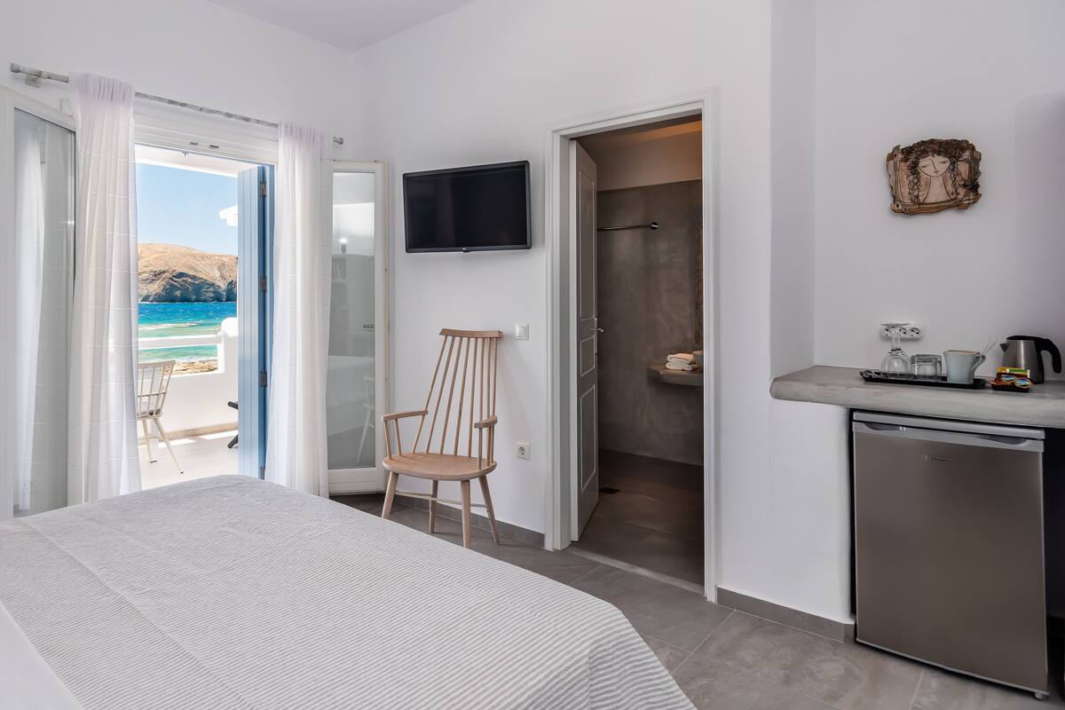 A bedroom with a bed, a chair, a TV, a shower, and a view of the sea.