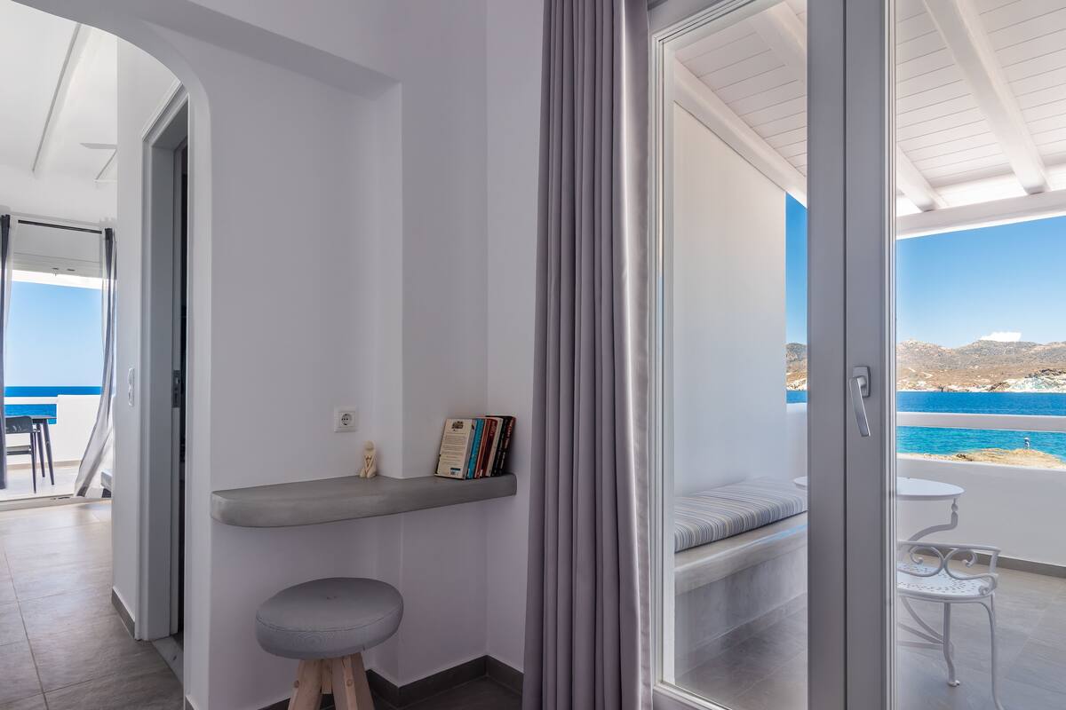A modern room with a balcony, a small seating area, and a view of the sea.