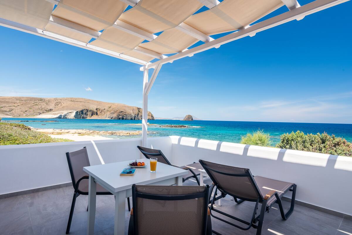 A terrace with a white table and chairs, overlooking a beach and the sea.