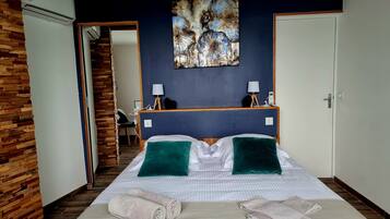 Een hotelkamer met een bed, twee groene kussens, een schilderij aan de muur, een bureau met een lamp en een stoel.