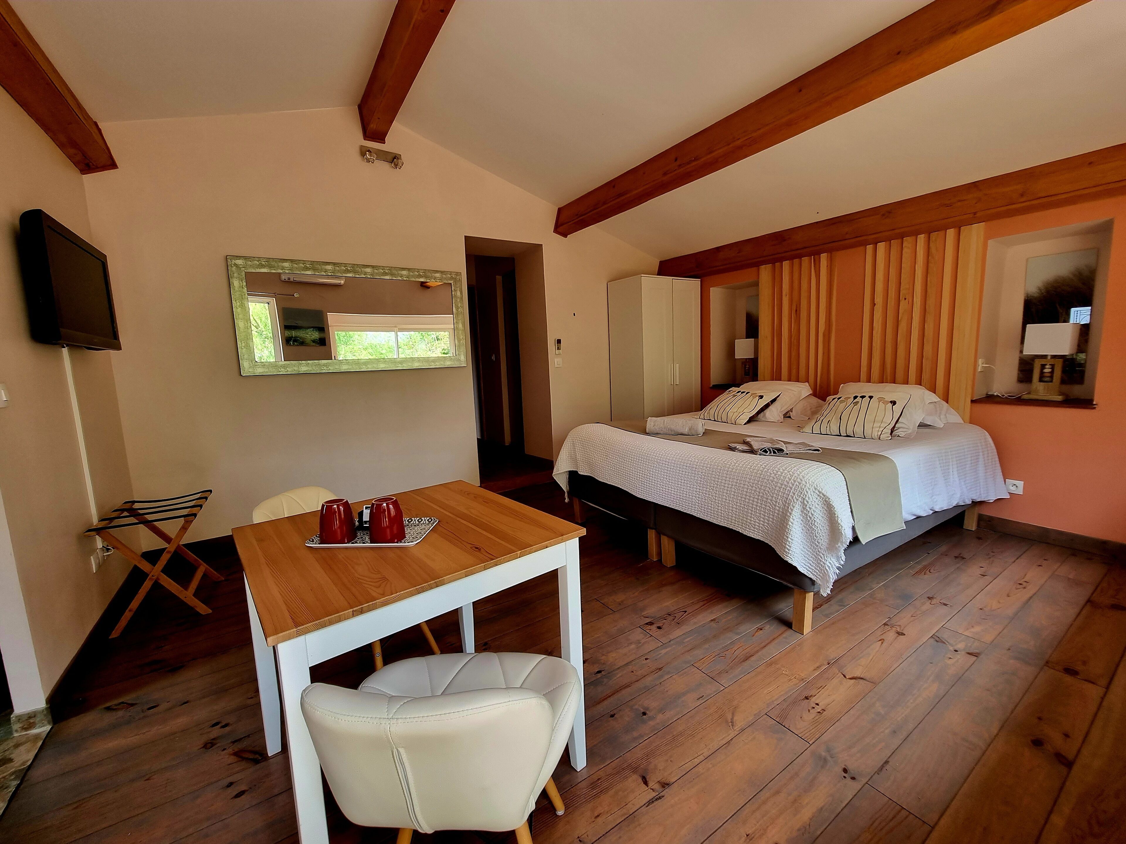 Un dormitorio con cama, una mesita de noche con dos tazas, una silla y un televisor montado en la pared.