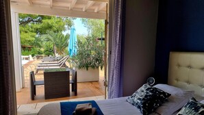 A bedroom with a bed, pillows, and a view of an outdoor patio with a pool, chairs, and umbrellas. - Villa Alyzea (Bessan)