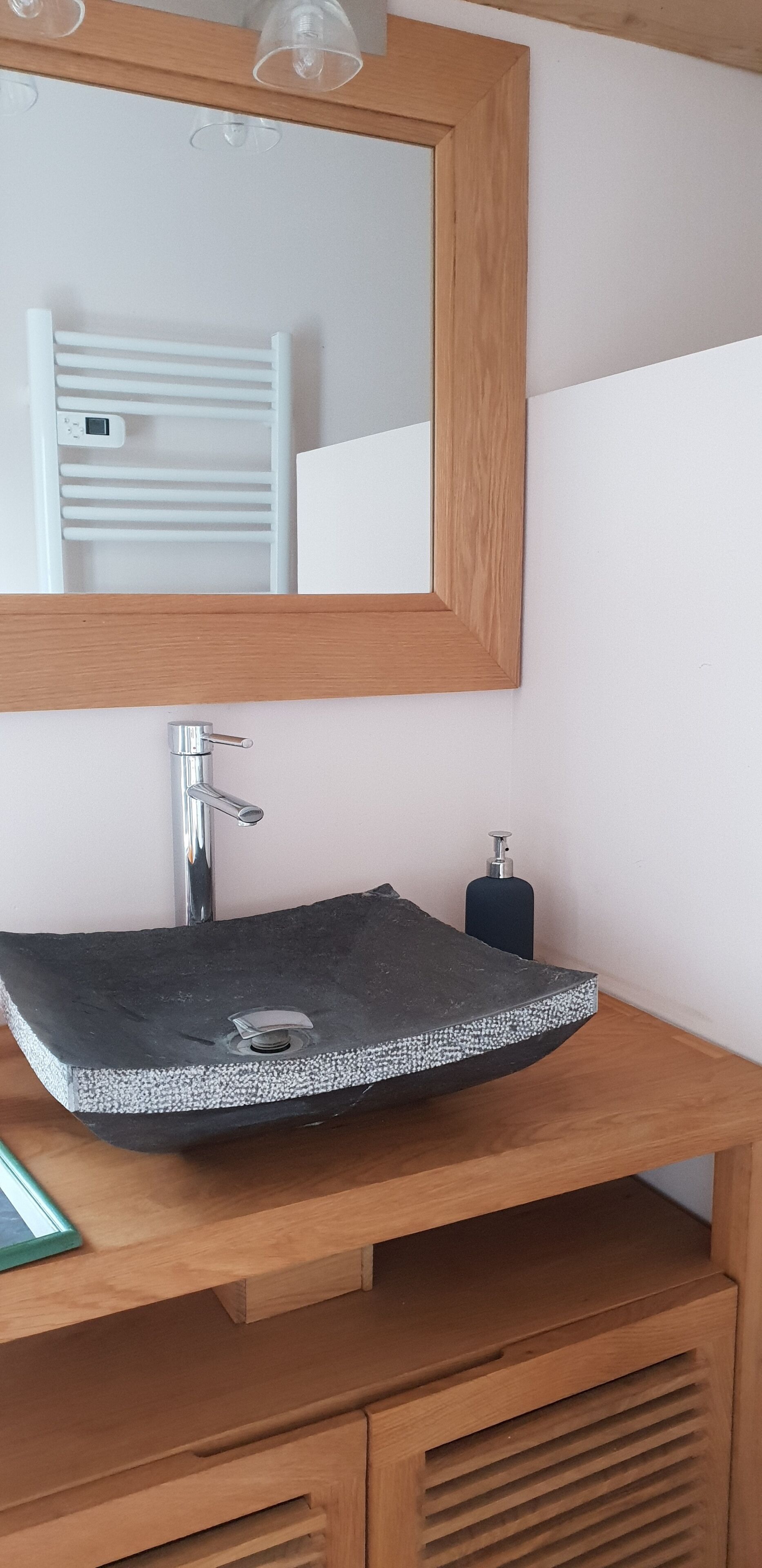 A bathroom with a wooden vanity, a black sink with a silver faucet, a mirror, and a soap dispenser.
