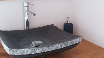 A bathroom with a wooden vanity, a black sink with a silver faucet, a mirror, and a soap dispenser.