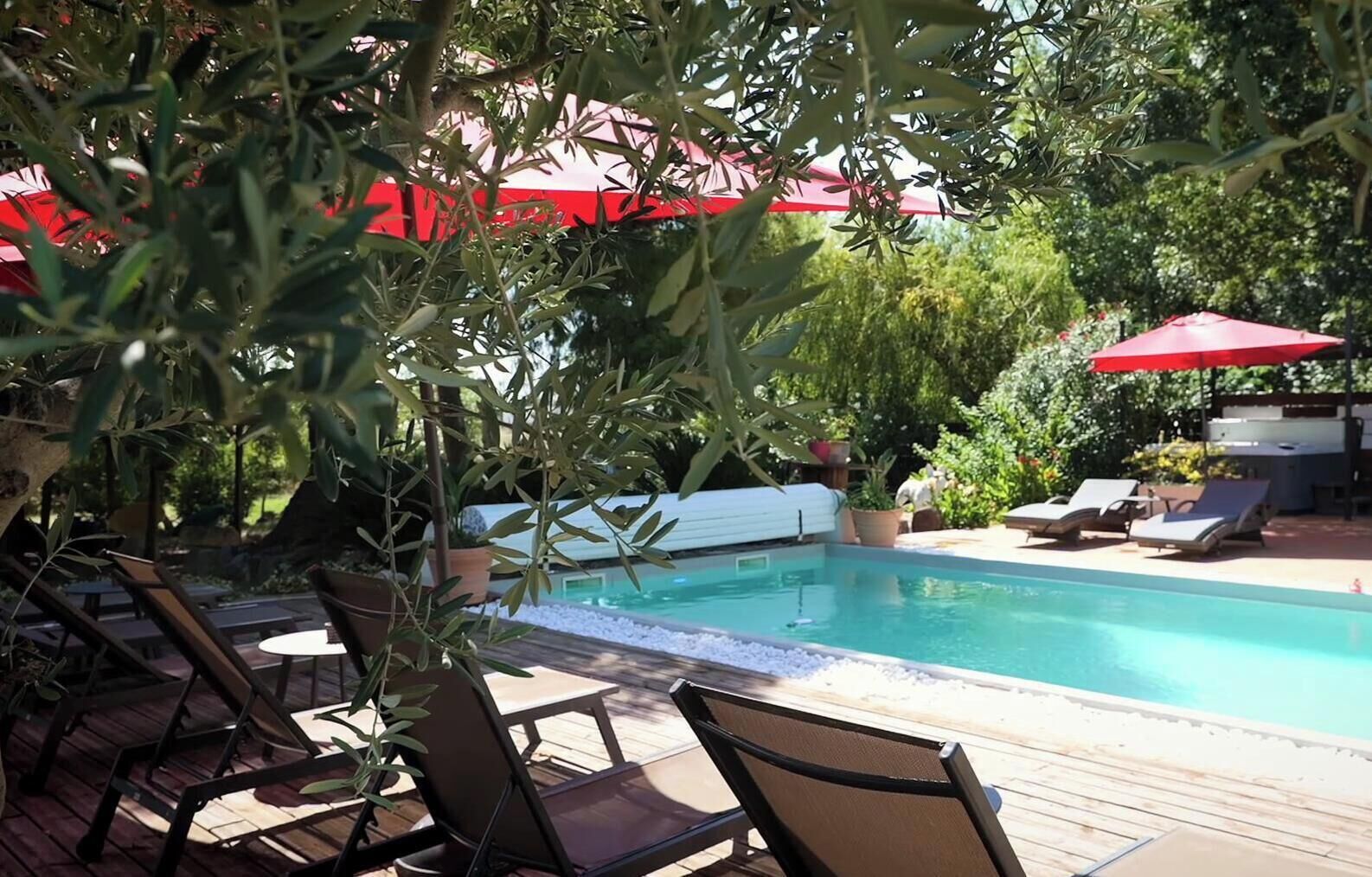 A pool area with lounge chairs and umbrellas, surrounded by greenery.