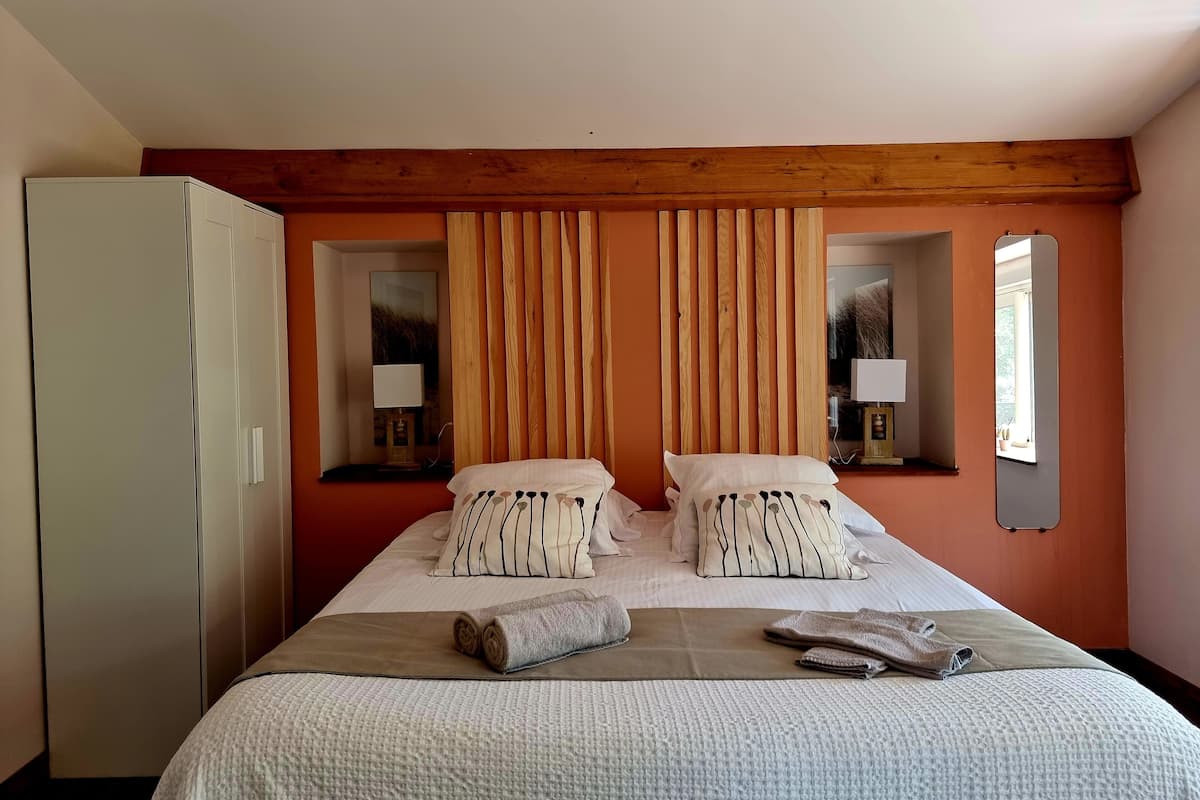 Habitación de hotel con cama, dos mesitas de noche con lámparas, armario y ventana con vistas.
