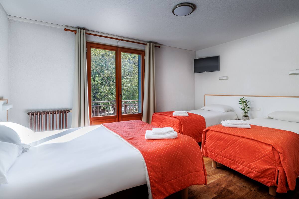 A hotel room with two beds, a TV, a window with curtains, and a radiator.
