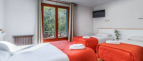 A hotel room with two beds, a TV, a window with curtains, and a radiator.
