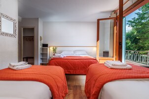 Habitación de hotel con dos camas, un armario, una mesita de noche y un ventanal con vistas a zonas verdes.