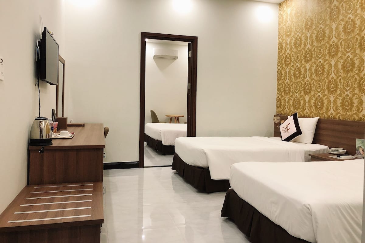 A hotel room with two beds, a desk with a kettle, a TV, and a mirror.