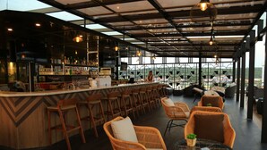 Eine moderne Bar mit einer Bar, Korbstühlen und Blick auf Gebäude durch große Fenster.