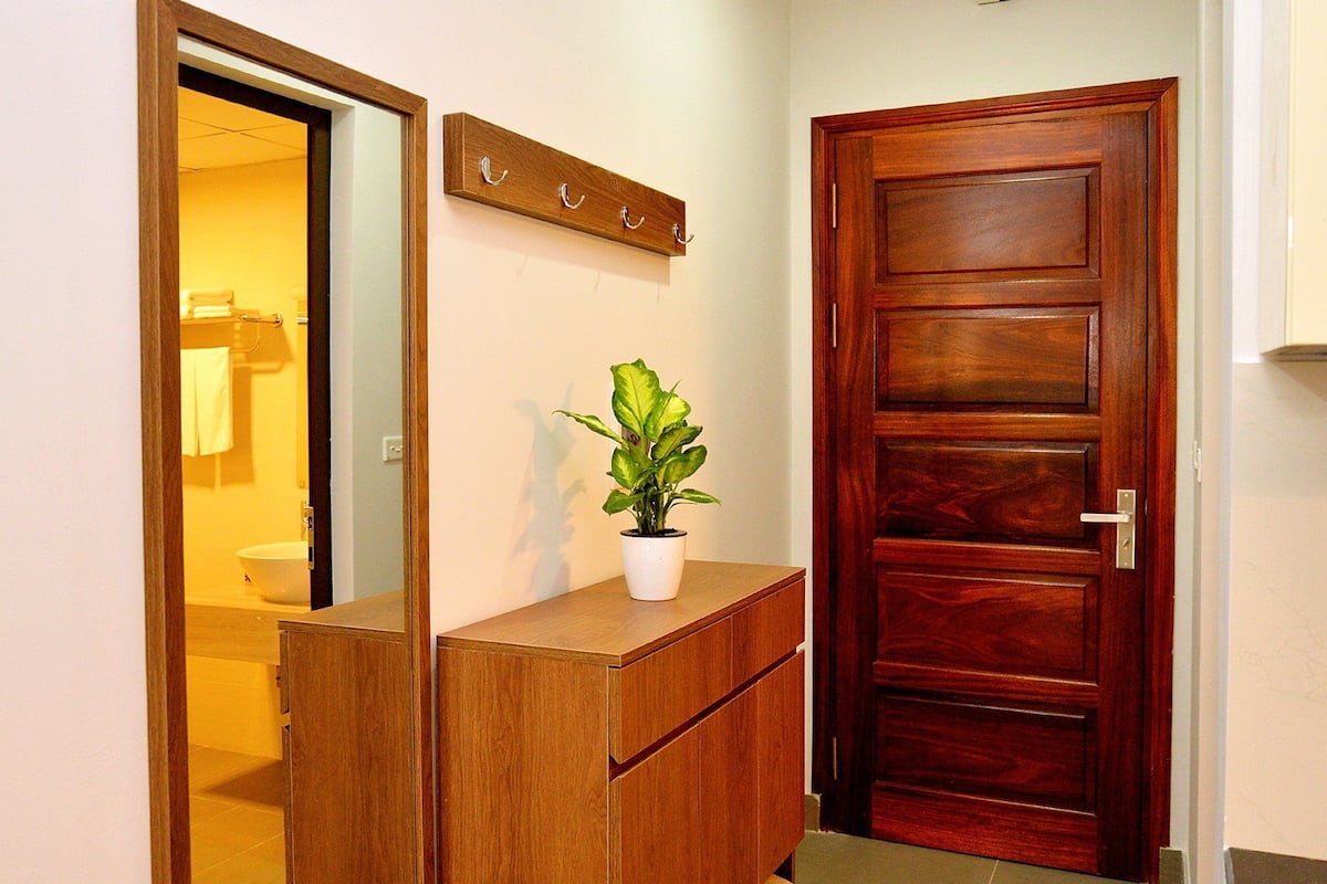 Eine Holztür mit Griff, ein Blumentopf auf einer Holztheke und ein Spiegel, der ein Badezimmer mit Waschbecken und Handtuchhalter reflektiert.