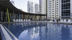 A swimming pool with lounge chairs and a covered area, surrounded by high-rise buildings. - Deluxe Holiday Homes - East Heights 1 (Dubai)