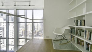 A modern room with large windows, a white rocking chair, and a bookshelf. - Deluxe Holiday Homes - East Heights 1 (Dubai)