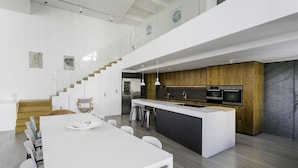 A modern kitchen with a central island, stainless steel appliances, and a wooden accent wall. - Deluxe Holiday Homes - East Heights 1 (Dubai)