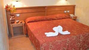 Een hotelkamer met een bed, nachtkastje, een vaas met bloemen en een lamp.