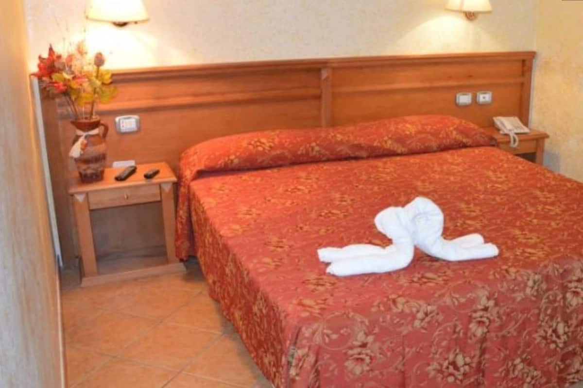 Une chambre d’hôtel avec un lit, une table de chevet, un vase de fleurs et une lampe.