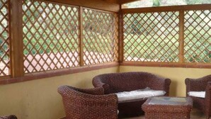 Een overdekt terras met rieten meubels en een lattenwand.