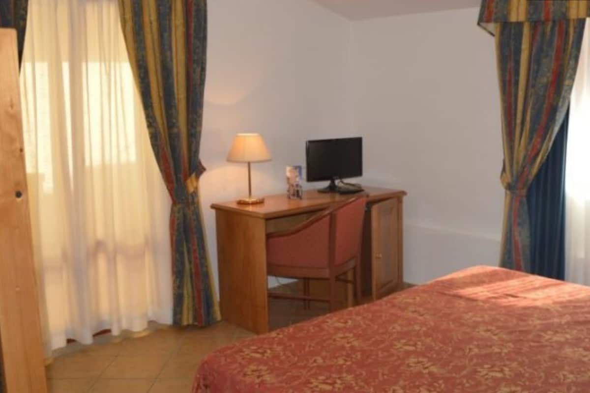 Une chambre à coucher avec un lit, un bureau avec une chaise, un ordinateur et des rideaux.