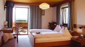 A hotel room with a bed, a sofa, a dining table, and a chair. There is a window with a view of the outdoors. - Hotel Oberhofer (Rio di Pusteria)