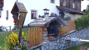 A stone wall with a wooden fence, a stone fireplace, and a wooden structure with a sloped roof. - Hotel Oberhofer (Rio di Pusteria)
