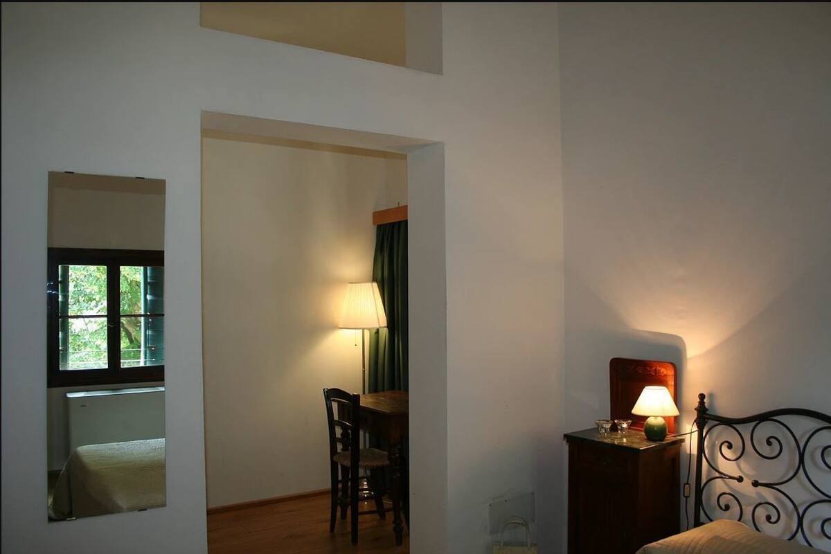 A room with a bed, a table with a lamp, a chair, and a window with curtains.