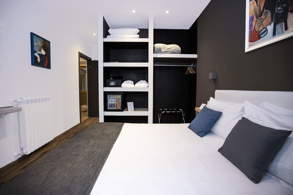A modern bedroom with a large bed, built-in shelving, a radiator, and a painting on the wall.