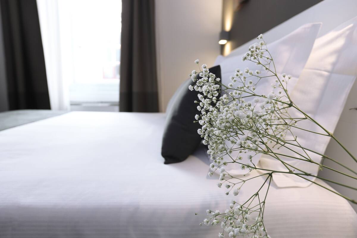 A neatly made bed with white linens and a single decorative branch of white flowers.